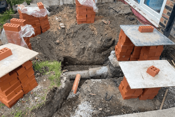 images shows pipes being laid outside in the ground at a property and 6 piles of orange bricks