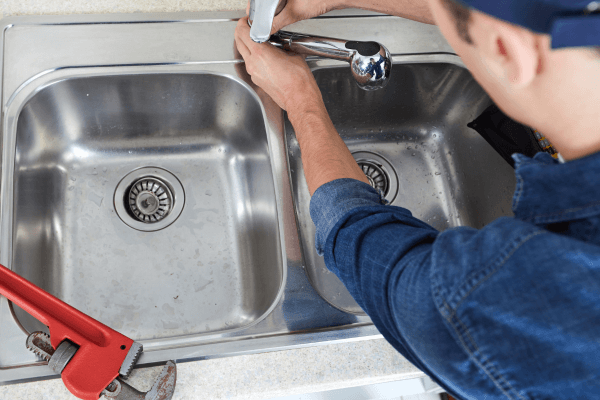 image shows a plumber fixing a kitchen sink tap a part of his planned Works and Reactive Maintenance in Social Housing service