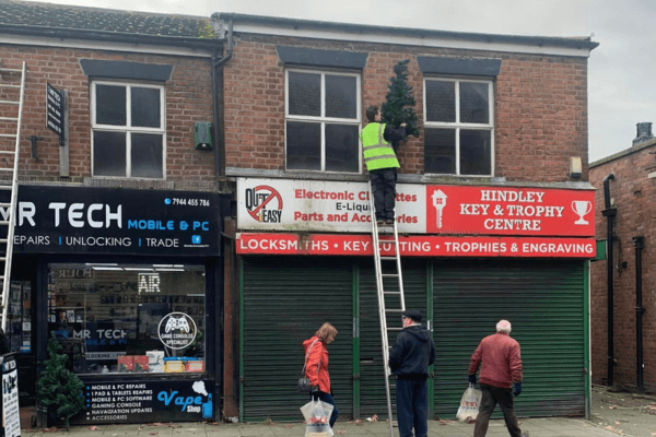 people are installing a Christmas tree in front of a shop