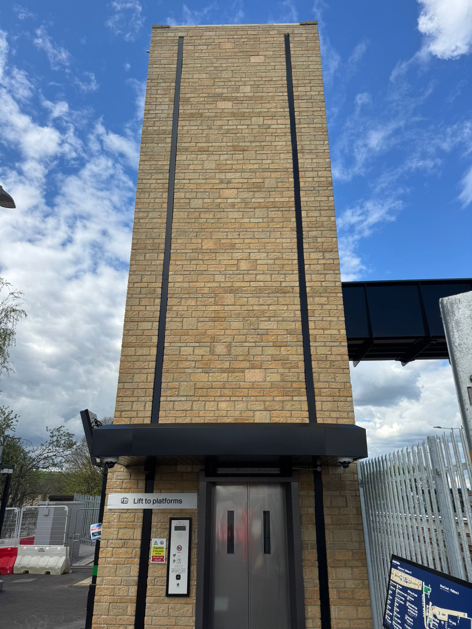 New lift tower constructed at Mirfield Station, featuring stone brick cladding, modern lift access to railway platforms, and a covered pedestrian bridge connection above.