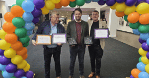 David Rothwell, Darren Stansfield and Scott Rothwell stood under a multi coloured balloon arch holding their certificates.